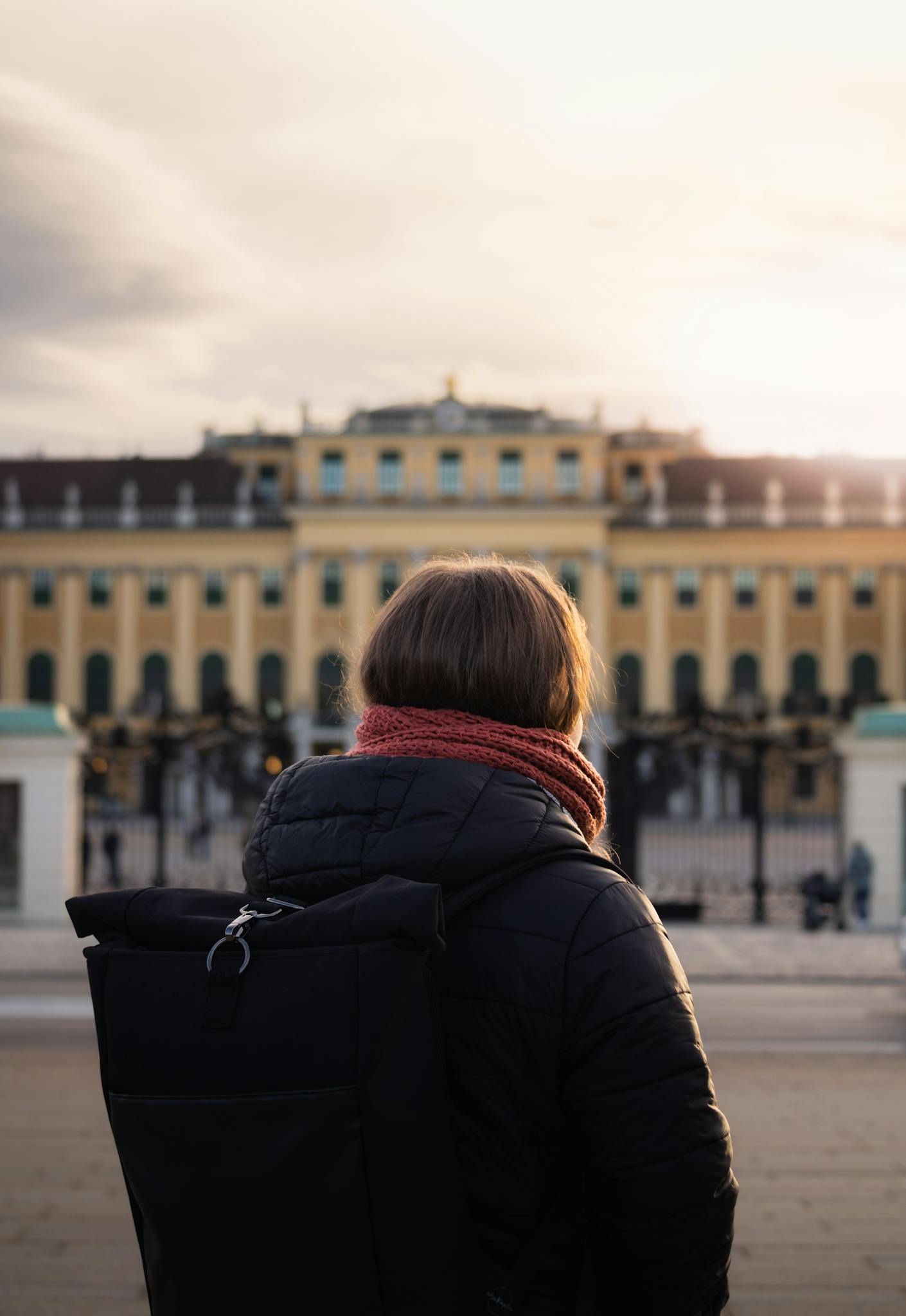 A woman stands before the historic Schönbrunn Palace in Vienna at sunset, capturing the architectural grandeur.