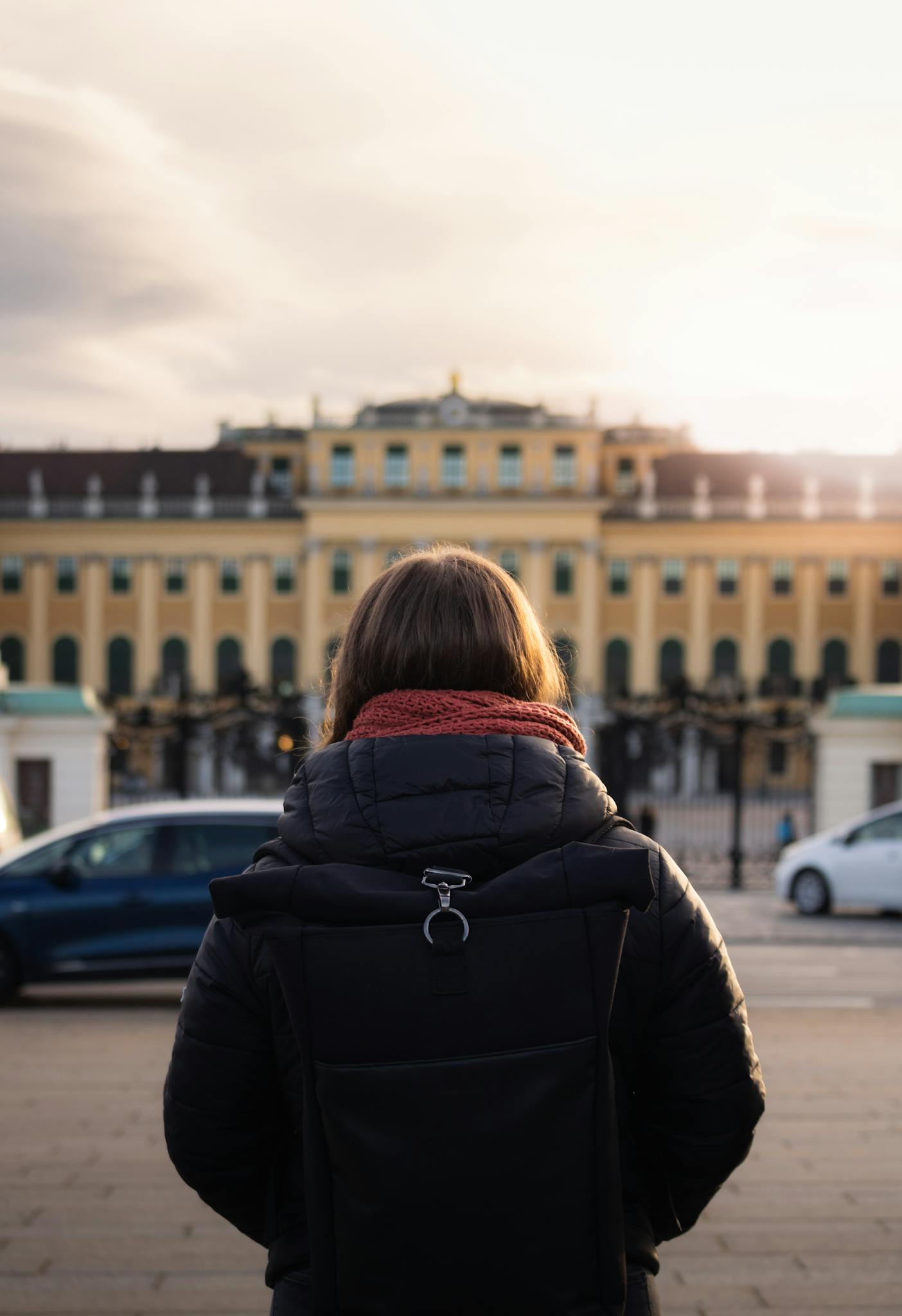 A woman stands in awe before the majestic Schönbrunn Palace in Vienna during sunset.